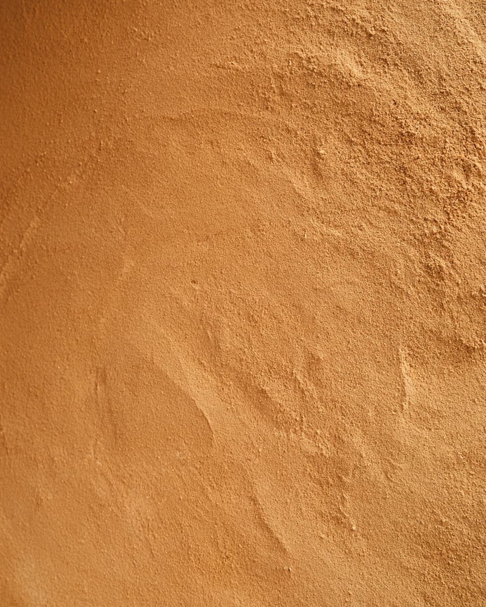 Close view of clay plaster in deep ochre, with a sandy, hand-worked surface