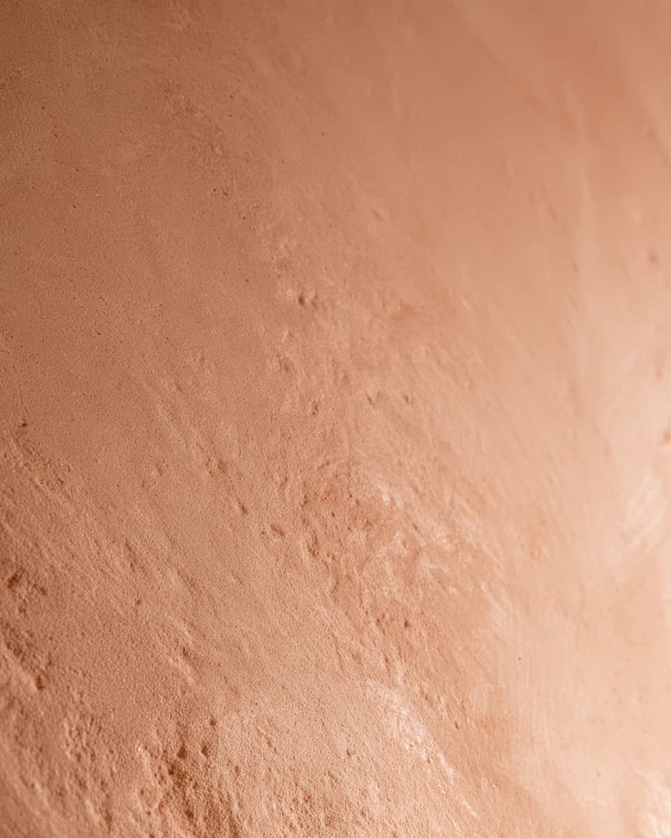 Close view of hand-troweled lime plaster in a warm terracotta pink, with soft trowel marks catching the light